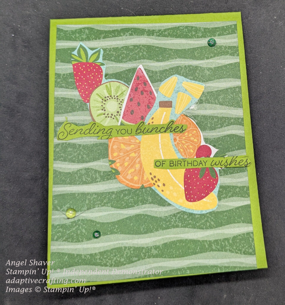 Green card with green striped patterned paper as card layer.  The center of the card has fruit cut from the patterned paper: strawberry kiwi, watermelon, pineapple chunks, orange slices, banana, and a cherry.  Sentiment says, "Sending you bunches of birthday wishes."