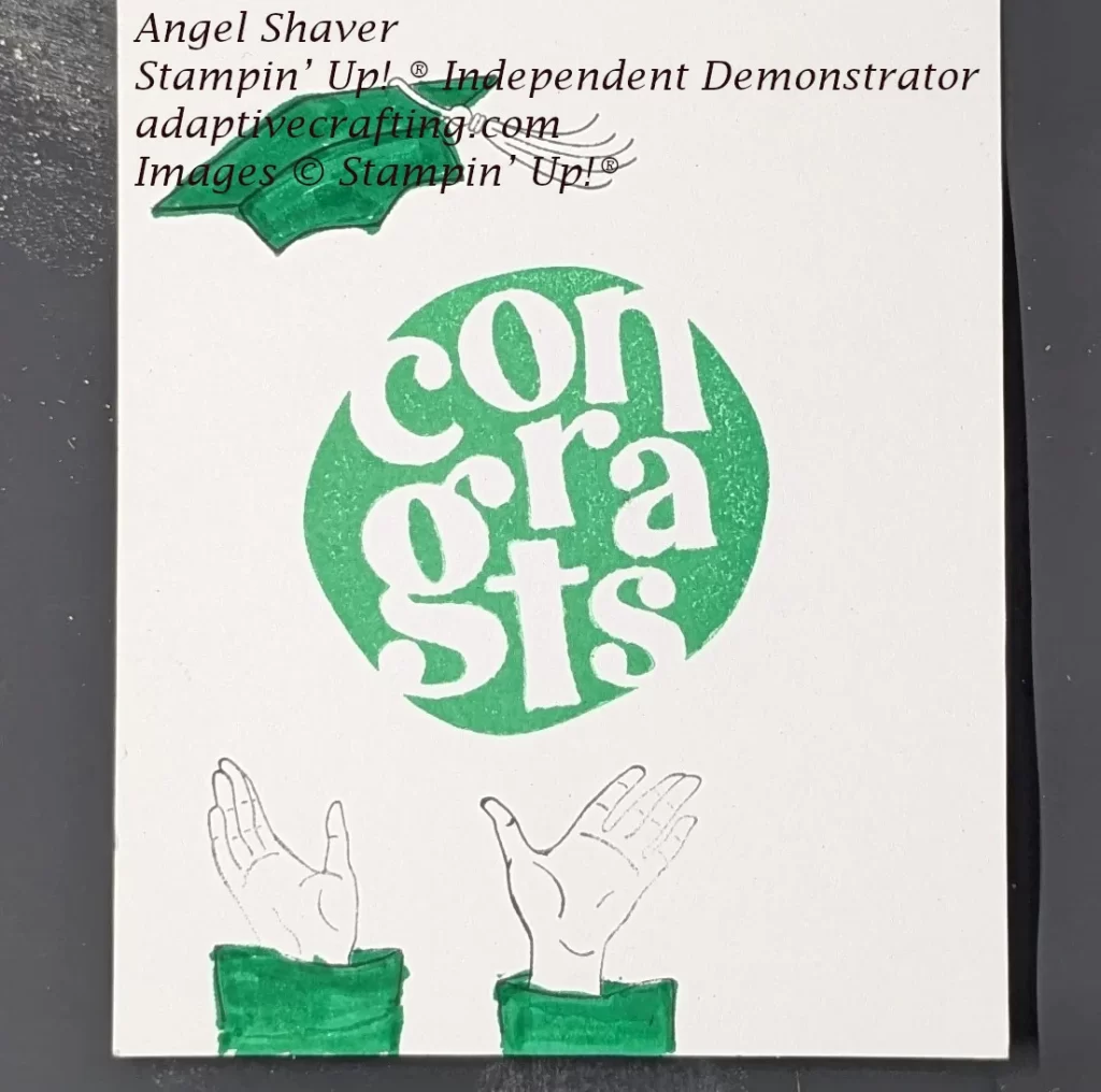 White inside of card. Green circle with white word stamped in the center of the card saying "Congrats." Stamped hands with green graduation gown stamped at bottom of page and looks like they are throwing green graduation cap up into the air. It is stamped at the top of the page.