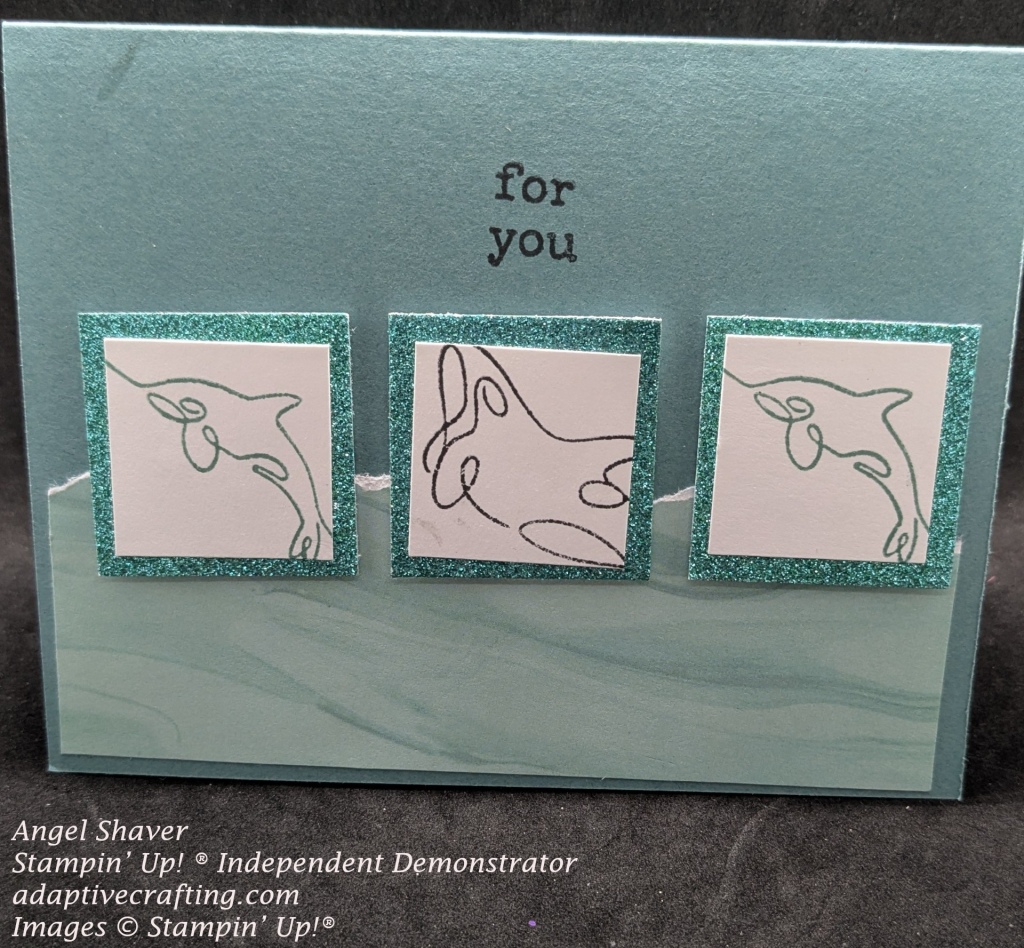 Teal card with patterned paper on bottom half of card front that looks like water.  Three square placed at top edge of water.  They are all white squares with stamped images framed with teal glitter paper.  The middle square features an orca.  The outside two are stamped with dophins.  Sentiment "for you," is stamped directly above orca square.