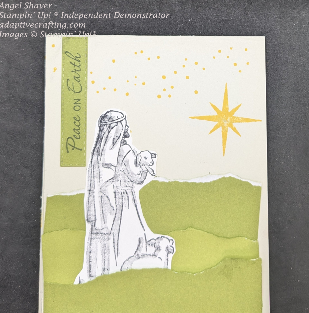 Beige card with torn paper layers at the bottom to create hills/landscape.  Stamped image of shepherd and sheep is nestled among the hills.  Stars, including large star are stamped in yellow on top of card.  Green rectangle is hanging from top of card and  says, "Peace on Earth."