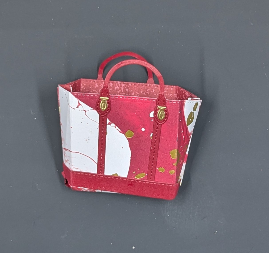 Red and white marbled diecut tote bag with gold flecks.  It has a red bottom, straps, and handles with gold fasteners.