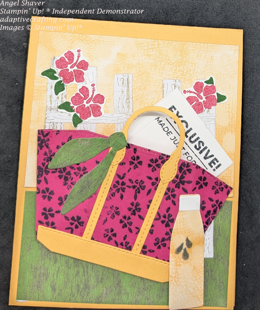 Peach card with peach patterrned paper on top of background and green patterend paper on the bottom. A white wood fence is in the middle of the page with a tote bag stamped will small flowers in front. There is a newspaper inside the tote bag that says, "Exclusive! Made just for you. There is a green scarf tied on the handle of the bag and a peach water bottle with stamped water droplets outside it. Pink tropical flowers decorate the fence.