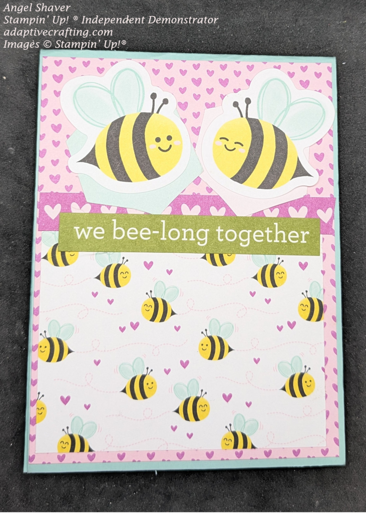 Blue card with pink patterned paper with purple hearts. Bottom half of card has patterned paper with bees and purple hearts. There is a strip of purple with pink hearts bout the patterned paper. Two sextuplet stickers are at the top of the card with a bee on each of them. Sentiment sticker says, "We bee-long together"