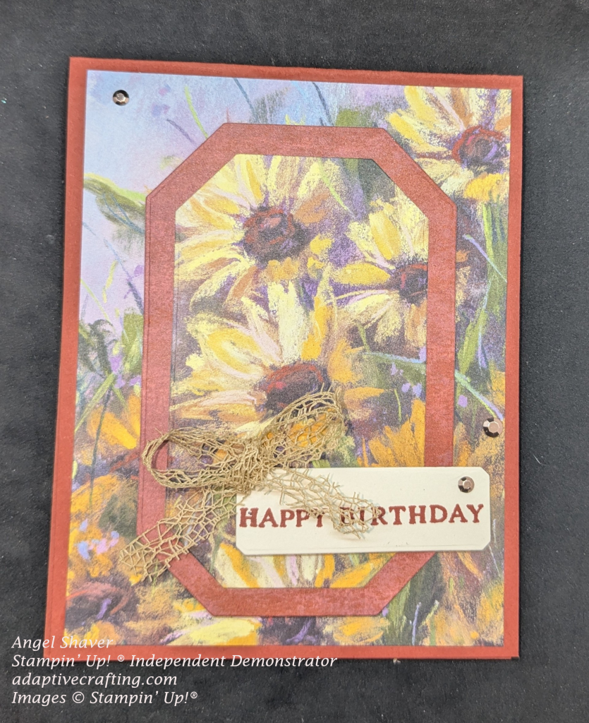 Rust colored card with sunflower patterned paper with center of patterned paper framed with rust colored cardstock.  Sentiment label says, "Happy Birthday".  There is a bow of loosely woven mesh and three copper embellishments.
