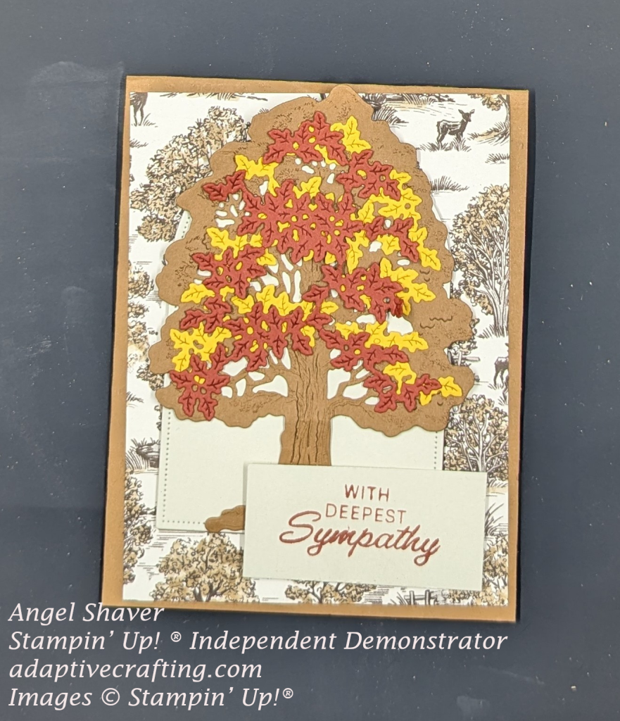Brown card with background paper printed with trees and deer.  Cream colored arched frame with die cut brown tree with orangish-red and yellow leaves on top  Sentiment label says "with deepest sympathy"