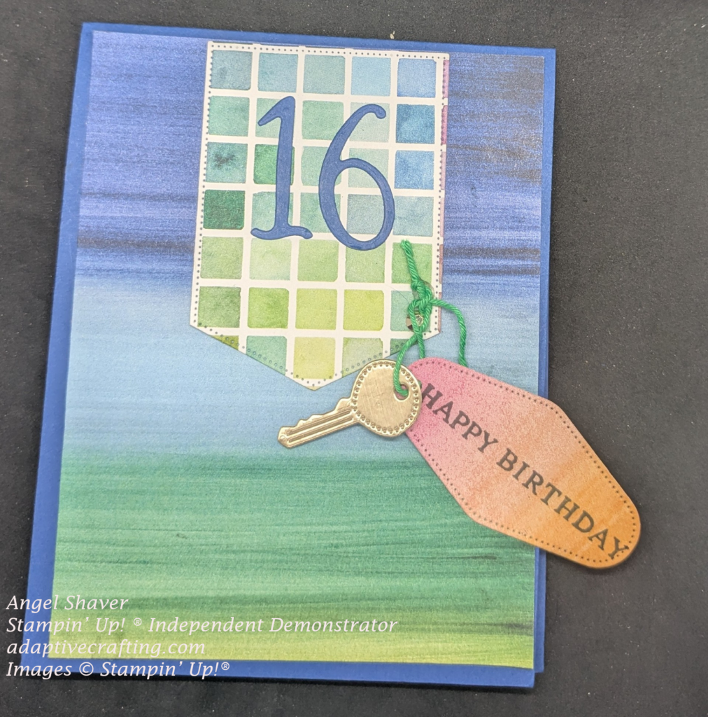 Blue card with blue and green front paper layer.  Banner hanging from top with blue and green sqaures and a blue 16 on it.  Gold key and pink and orange key ring that says, "Happy Birthday" is attached with green twine