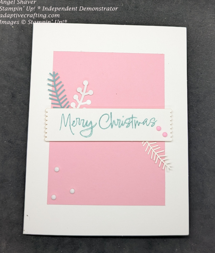 White card with pink smaller rectangle layer on top. On top of the pink rectangle is a sentiment label stamped with "Merry Christmas" n teal.  With teal and white branches sticking out from behind the label.  Decorated with pink and white dots.