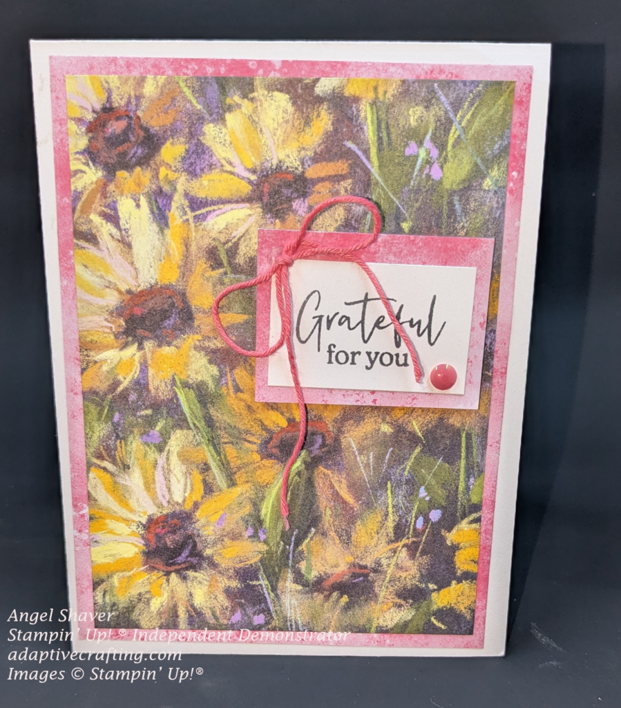 White card with layer of pink paper.  Then, a layer of patterned paper featuring sunflowers on top of that.  The sentiment label is a white rectangle that says, "Grateful for you" framed by pink paper.  There is a pink bow and one pink enamel dot on the sentiment label.