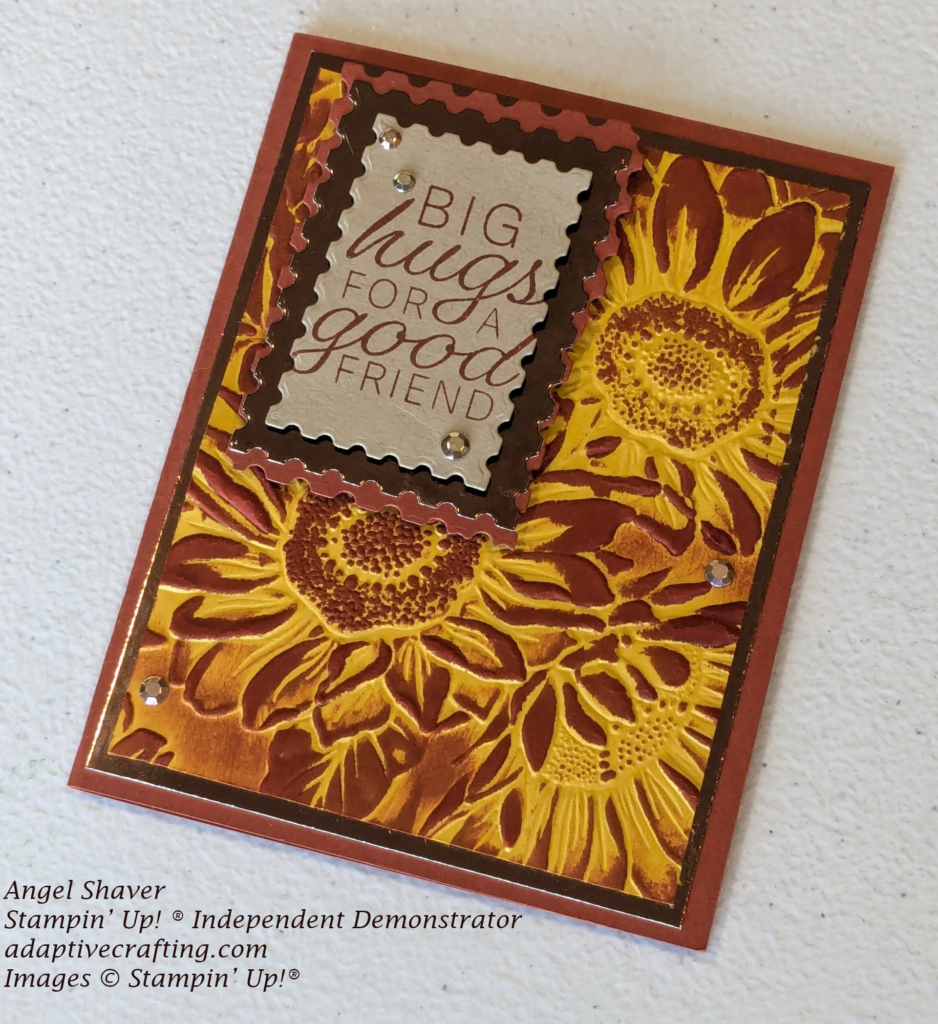 Rust colored card with layer of earthen colored foil and yellow cardstock embossed with sunflowers and inked with rust colored ink.  Sentiment tag is light brown framed with foil and rust colored cardstock.  Sentiment says, "Big hugs for a good friend"