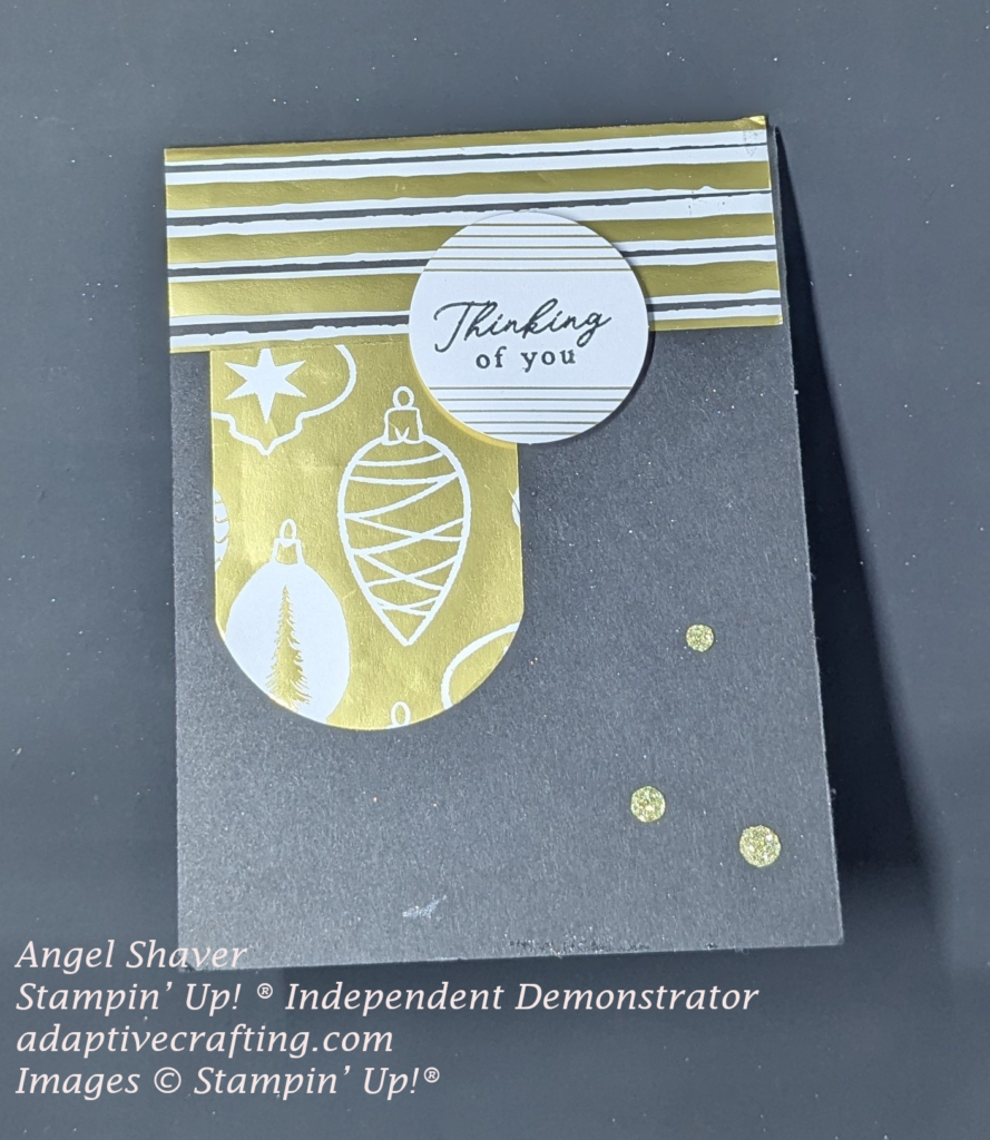 Black card with gold, white, and striped patterned paper at top of card. gold banner with white ornaments printed on it. White circle with gold stripes and sentiment that says, "Thinking of you" Embellished with gold sequins,
