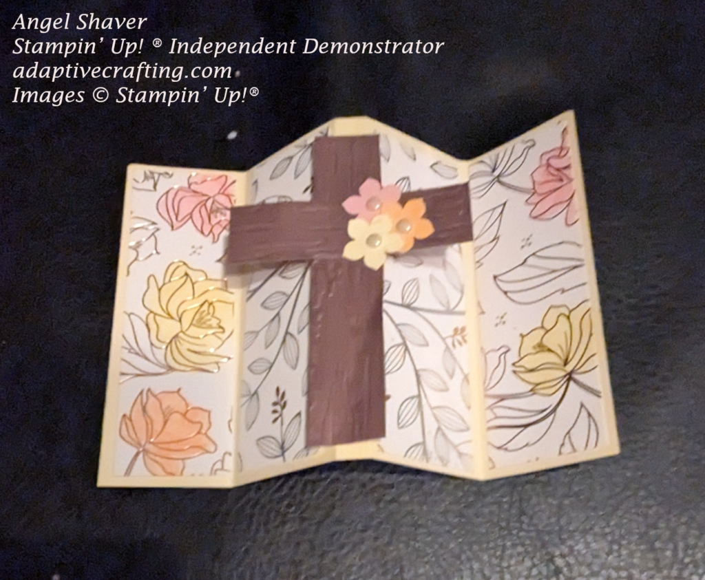 Yellow "M" folded card with strips of patterned paper featuring foil outlined foliage and flowers.  Some of the flowers were colored in with pink, yellow, and peach markers.  The focal point image is a cross made of two strips of woodtone paper embossed with a Birch wood embossing folder.  Three punched flowers--pink, yellow, and peach are added to the front of the cross with vintage pearl centers.