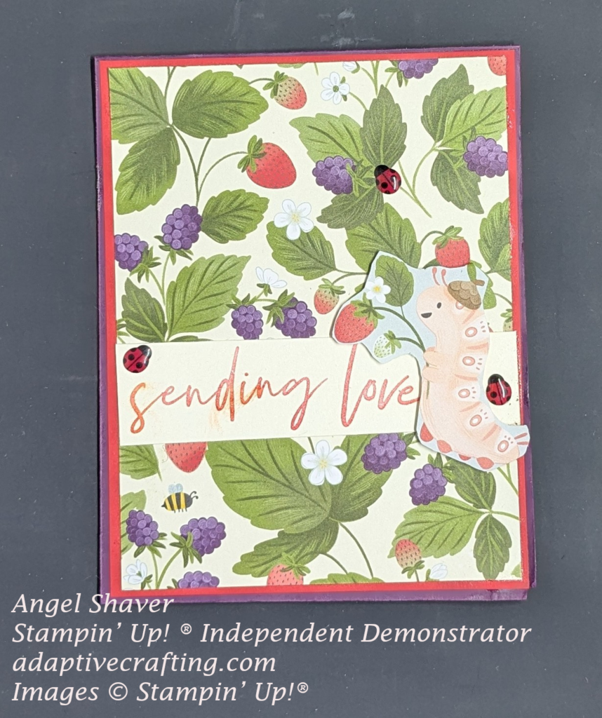 Purple card with layer of red cardstock and then layer of patterned paper printed with strawberry and blackberry plants.  Strip of cardstock across card front is stamped with "sending love."  Pink caterpillar holding strawberry plant is at end of sentiment.  Card front decorated with ladybug embellishments.