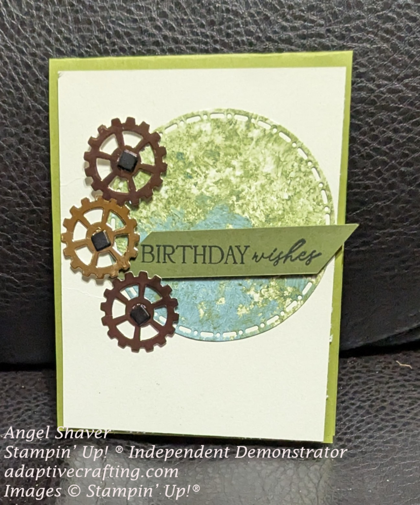 Green card with beige card front layer.  A large circle created from green and blue patterned paper.  There are three metallic gears around the circle attached with brads.  A green sentiment label is across large circle and says "Birthday wishes"