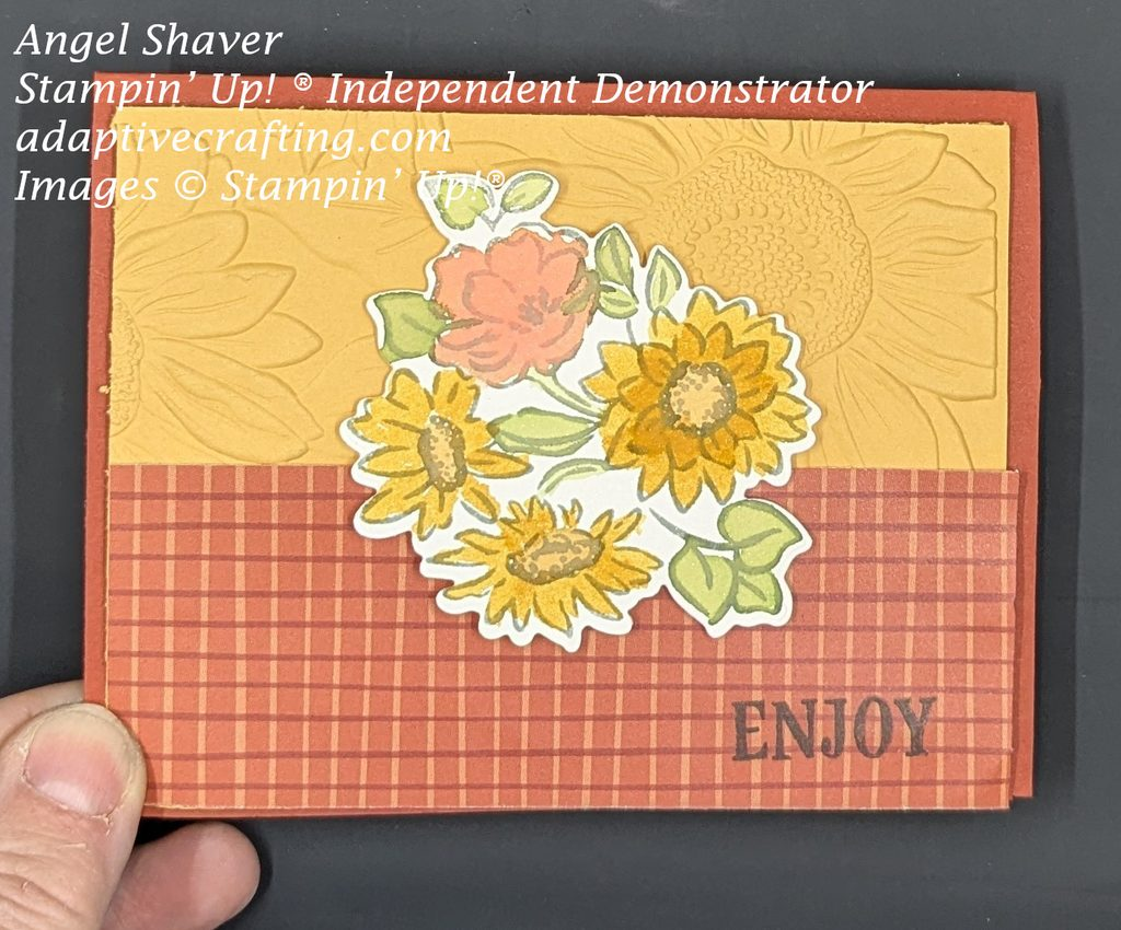 Rust orange colored card base.  Layer on top half of the card is yellow cardstock embossed with sunflowers.  Bottom half is a rust color plaid with thin brown and yellow lines.  Featured image is bundle of fall flowers, watercolored.  "Enjoy" is stamped in black at the bottom of the card.